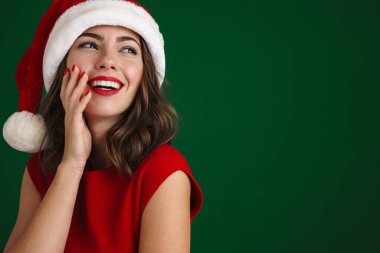 Geleneksel Noel kostümü giyen gülümseyen genç ve güzel bir kadının yeşil arka planda tek başına dikilirken yakın plan.