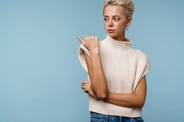 Ciddi güzel sarışın kız mavi arka planda izole edilmiş bir şekilde işaret ediyor.