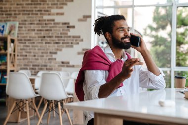 Gülümseyen Afrikalı Amerikalı adam cep telefonuyla konuşuyor ve ofiste çalışıyor.