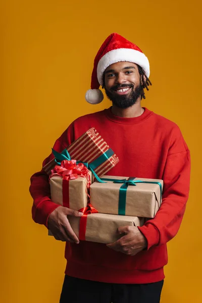 戴着圣诞老人帽 头戴黄色背景的圣诞礼物的快乐的非洲裔美国人 — 图库照片