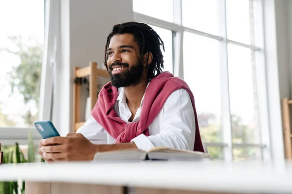 Χαρούμενος Αφροαμερικάνος Που Χαμογελάει Και Χρησιμοποιεί Κινητό Ενώ Δουλεύει Στο — Φωτογραφία Αρχείου