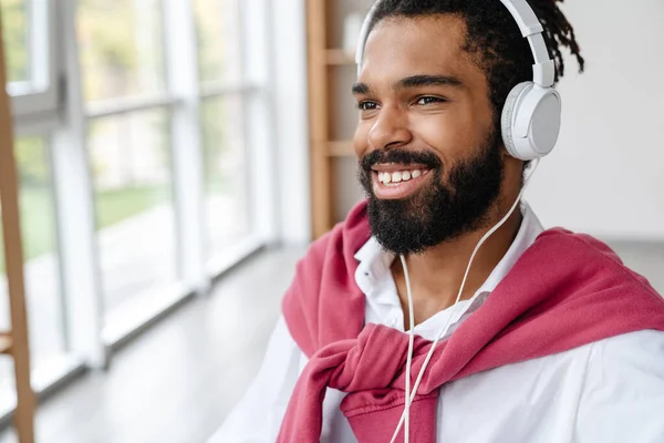 陽気なアフリカ系アメリカ人の男笑顔とオフィスでヘッドフォンで音楽を聴く — ストック写真