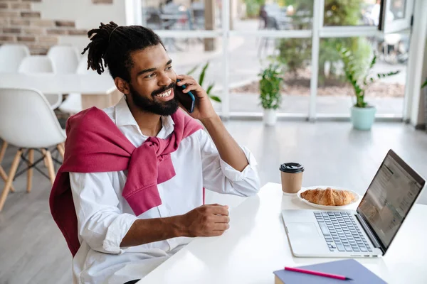 Усміхнений Афроамериканський Хлопець Розмовляє Мобільному Телефоні Працює Ноутбуком Офісі — стокове фото