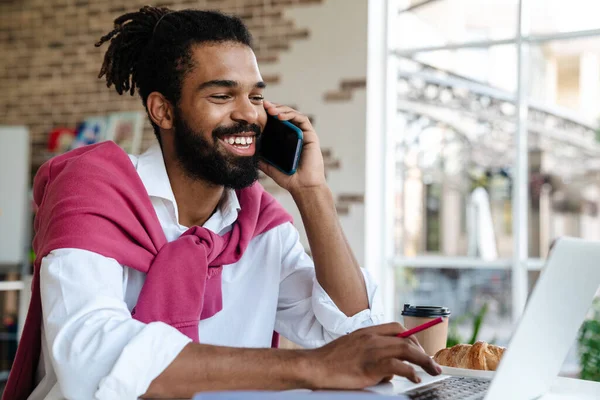 Uśmiechnięty Afroamerykanin Rozmawiający Przez Telefon Komórkowy Pracujący Laptopem Biurze — Zdjęcie stockowe