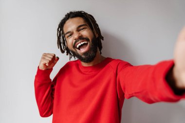 Heyecanlı Afrikalı Amerikalı adam beyaz arka planda izole edilmiş selfie çekerken kazanan hareketi yapıyor.