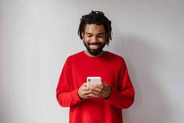 Gri arka planda cep telefonuyla izole edilmiş gülümseyen Afrikalı genç bir adamın portresi.