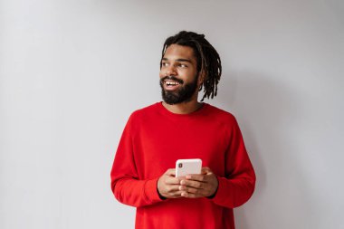 Gri arka planda cep telefonuyla izole edilmiş gülümseyen Afrikalı genç bir adamın portresi.