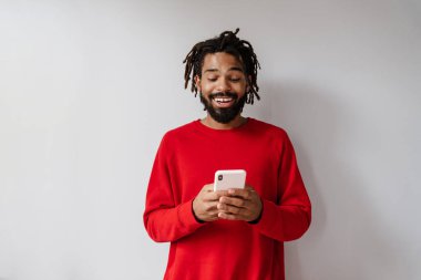 Gri arka planda cep telefonuyla izole edilmiş gülümseyen Afrikalı genç bir adamın portresi.