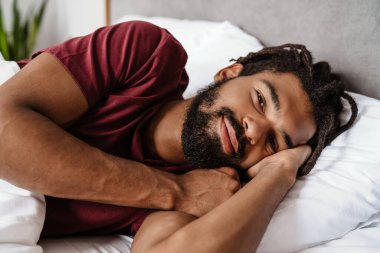 Memnuniyetle Afro-Amerikalı adam kameraya gülümserken evde uyuduktan sonra yatakta yatıyordu.