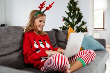 Evdeki kanepede otururken oyuncak geyik boynuzu takan mutlu bir kız.