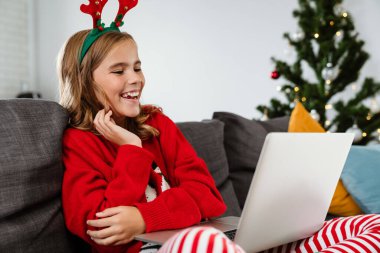 Evdeki kanepede otururken oyuncak geyik boynuzu takan mutlu bir kız.