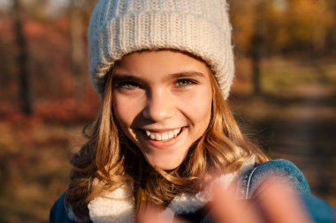 Sonbahar parkında gezen neşeli genç bir kız resmi.