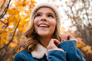 Sonbahar parkında gezen neşeli genç bir kız resmi.