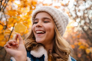 Sonbahar parkında elinde yaprakla gezen iyimser genç bir kız görüntüsü.