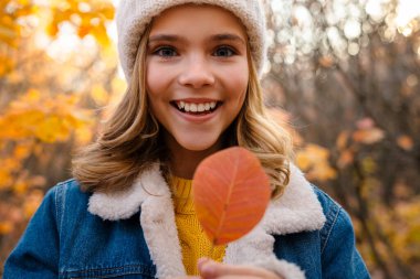 Güz parkında elinde yaprakla gezen güzel, pozitif bir kız resmi.