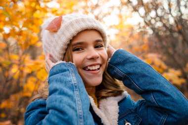 Sonbahar parkında gezen neşeli genç bir kız resmi.