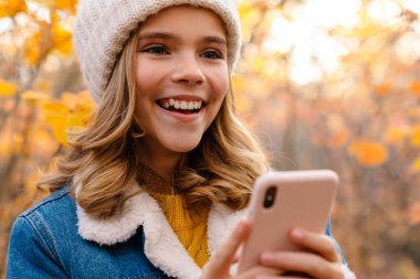 Sonbahar parkında cep telefonu kullanan genç pozitif bir kızın görüntüsü