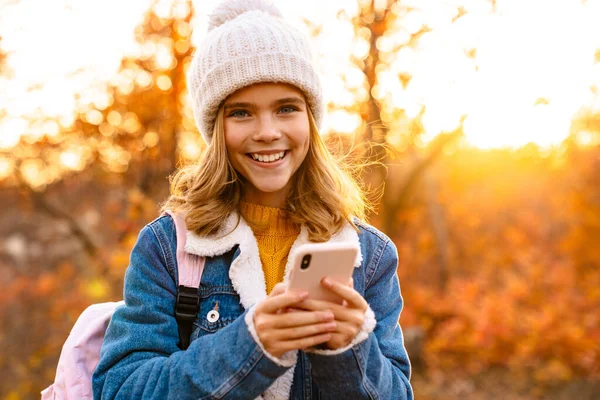 Mosolygó Kislány Őszi Ruhát Visel Sétál Parkban Mobiltelefonnal — Stock Fotó