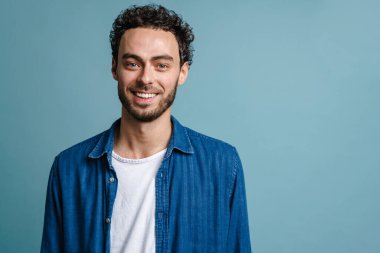 Neşeli yakışıklı adam gülümsüyor ve mavi arka planda izole edilmiş kameraya bakıyor.