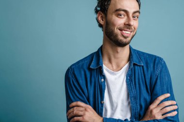 Gülümseyen ve elleri çapraz pozlar veren neşeli yakışıklı adam mavi arka planda izole edilmiş.