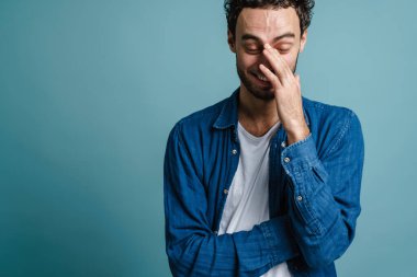 Komik yakışıklı adam gülüyor ve yüzünü mavi arka planda gizliyor.