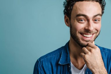 Mutlu yakışıklı adam gülümsüyor ve mavi arka planda izole edilmiş kameraya bakıyor.