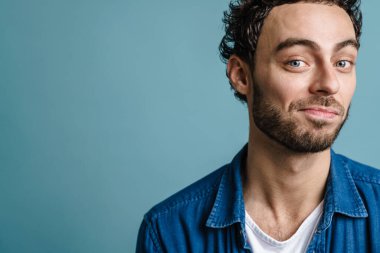 Mutlu yakışıklı adam gülümsüyor ve mavi arka planda izole edilmiş kameraya bakıyor.