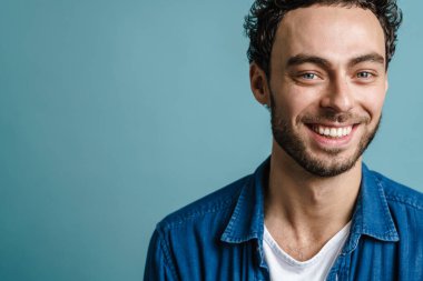 Mutlu yakışıklı adam gülümsüyor ve mavi arka planda izole edilmiş kameraya bakıyor.