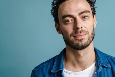 Mavi arka planda izole edilmiş, poz veren ve kameraya bakan yakışıklı adam.