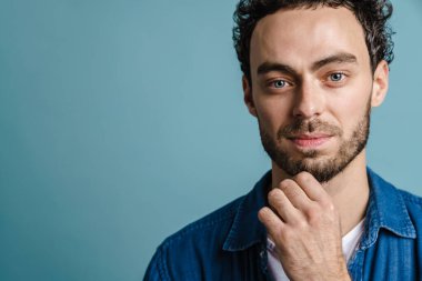 Mavi arka planda izole edilmiş, poz veren ve kameraya bakan yakışıklı adam.