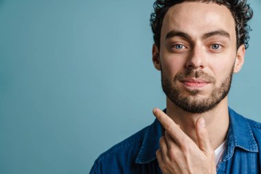 Mavi arka planda izole edilmiş, poz veren ve kameraya bakan yakışıklı adam.