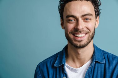 Mutlu yakışıklı adam gülüyor ve mavi arka planda izole edilmiş kameraya bakıyor.