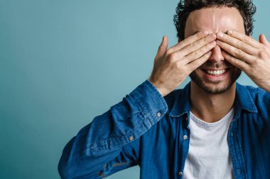 Gülümseyen ve gözlerini kapatan neşeli yakışıklı adam mavi arka planda izole edilmiş.