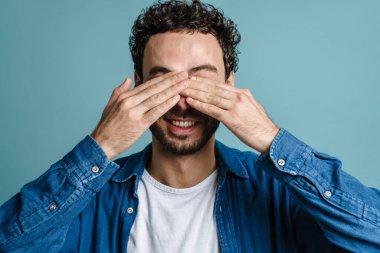 Gülümseyen ve gözlerini kapatan neşeli yakışıklı adam mavi arka planda izole edilmiş.