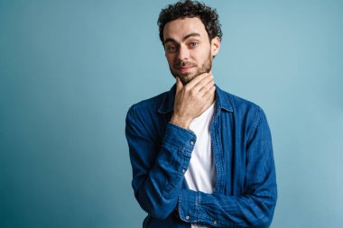 Mavi arka planda izole edilmiş, poz veren ve kameraya bakan yakışıklı adam.