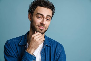 Mavi arka planda izole edilmiş, poz veren ve kameraya bakan yakışıklı adam.