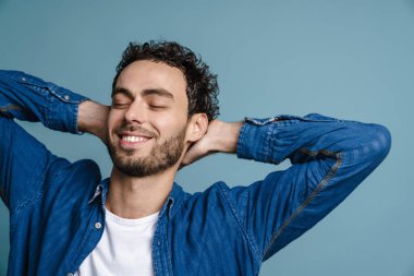 Mavi arka planda, elleri boynunun arkasında bağlı poz veren mutlu yakışıklı adam.