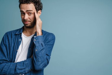 Kafası karışmış yakışıklı adam poz veriyor ve mavi arka planda izole edilmiş kameraya bakıyor.