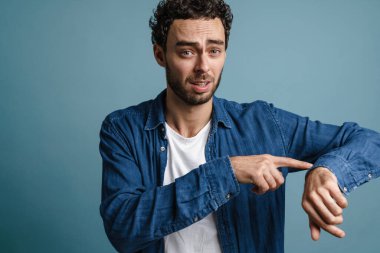 Sinirli yakışıklı adam mavi arka planda kafasını işaret ediyor.