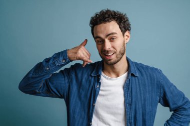 Gülümseyen genç adam mavi arka planda izole edilmiş bir işaret gösteriyor.