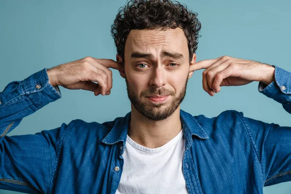 Blank Ongelukkige Man Poseren Pluggen Zijn Oren Geïsoleerd Blauwe Achtergrond — Stockfoto