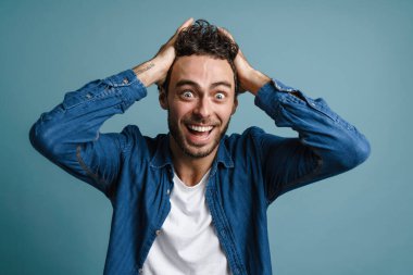 Mutlu genç adam başarıyı mavi arka planda kutluyor, kameraya bakıyor.