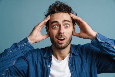 Şok olmuş beyaz adam mavi arka planda mahsur kalmış kamerada şaşkınlığını ifade ediyor.