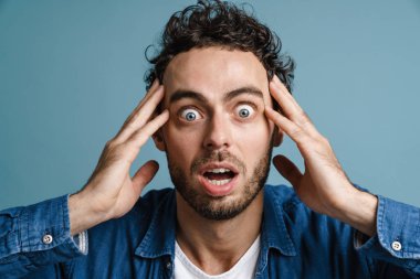 Şok olmuş beyaz adam mavi arka planda mahsur kalmış kamerada şaşkınlığını ifade ediyor.