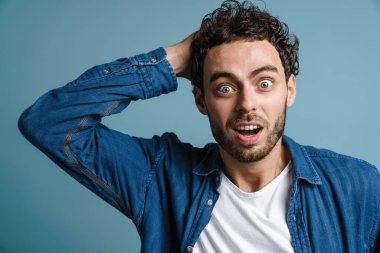 Heyecanlı beyaz adam mavi arka planda mahsur kalmış kamerada şaşırdığını ifade ediyor.