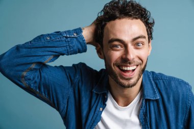 Mutlu yakışıklı adam gülüyor ve mavi arka planda izole edilmiş kameraya bakıyor.