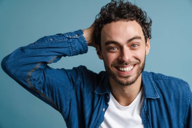 Mutlu yakışıklı adam gülüyor ve mavi arka planda izole edilmiş kameraya bakıyor.