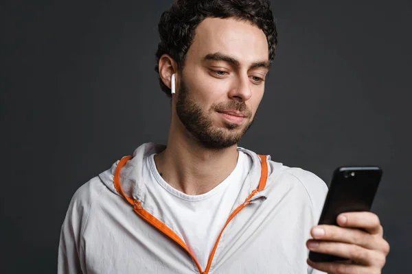 没有刮胡子的帅哥在无线耳机使用手机隔离灰色背景 — 图库照片