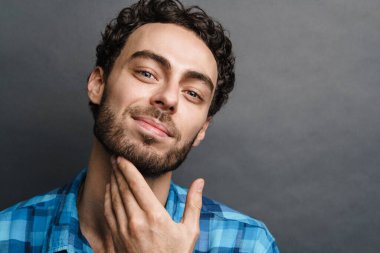 Gri arka planda izole edilmiş gülümseyen ve poz veren neşeli yakışıklı adam.