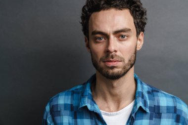 Tıraşsız yakışıklı adam gri arka planda kameraya bakıyor ve poz veriyor.